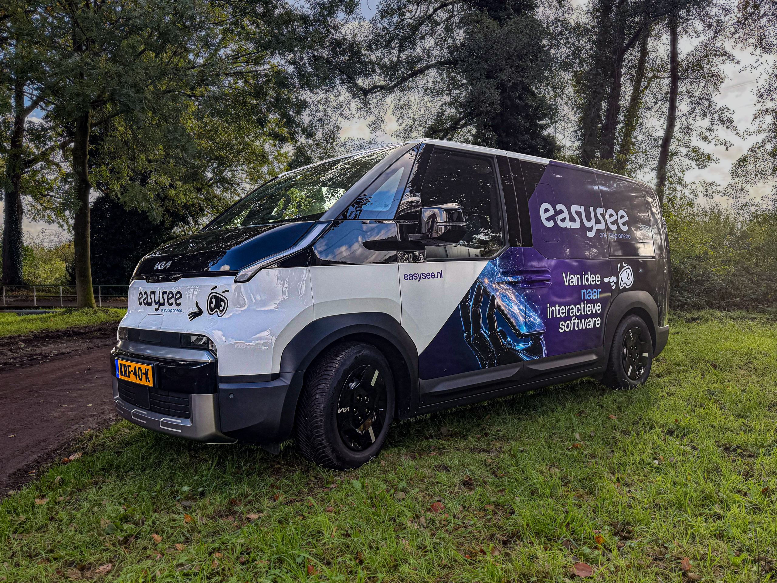 De nieuwe elektrische bedrijfswagen van Easysee, strak gewrapt met een paarse graphic, het logo en de tekst 'Van idee naar interactieve software', geparkeerd op het gras.